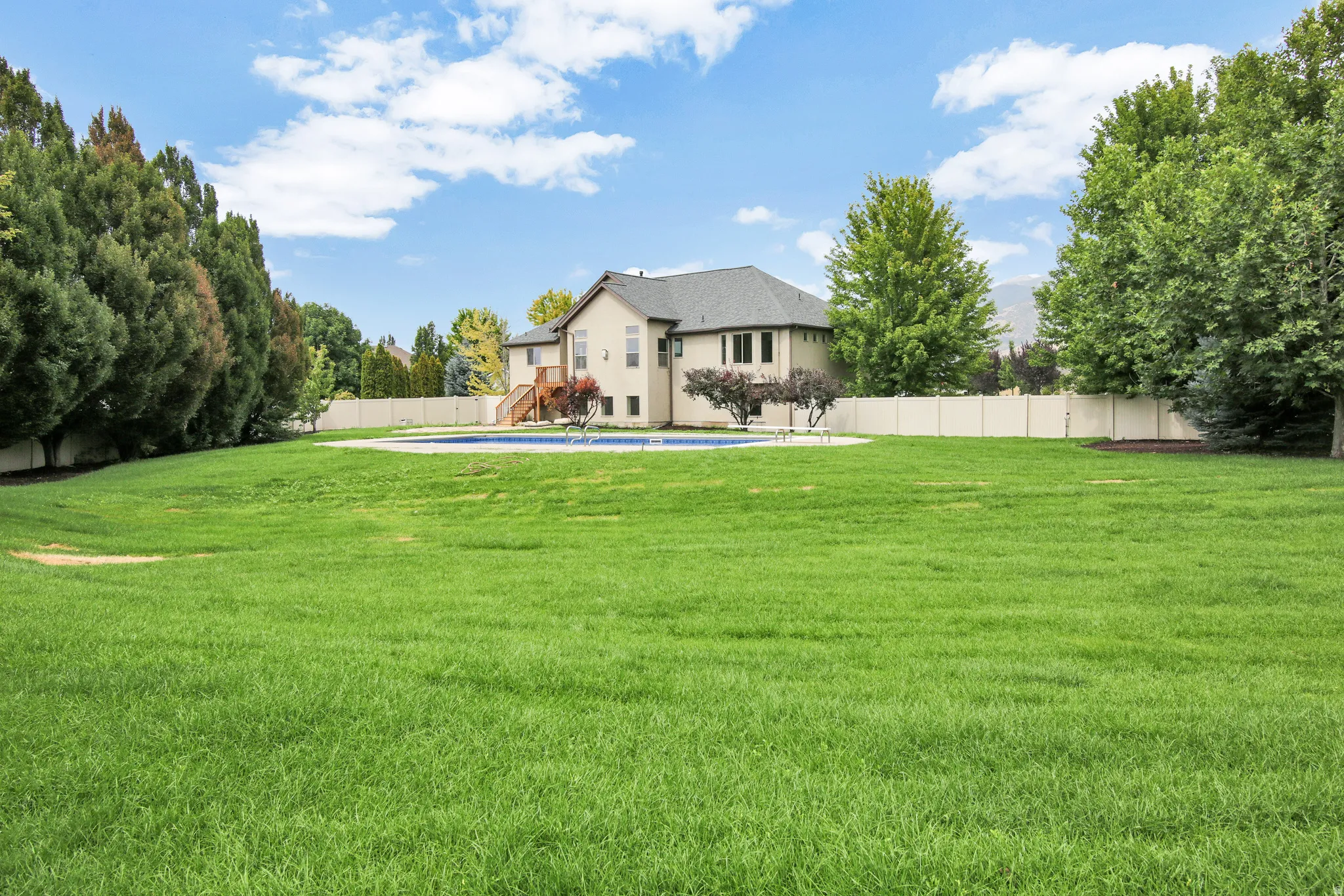Expansive lawn featuring a swimming pool, privacy fencing, mature trees, and a two-story residence