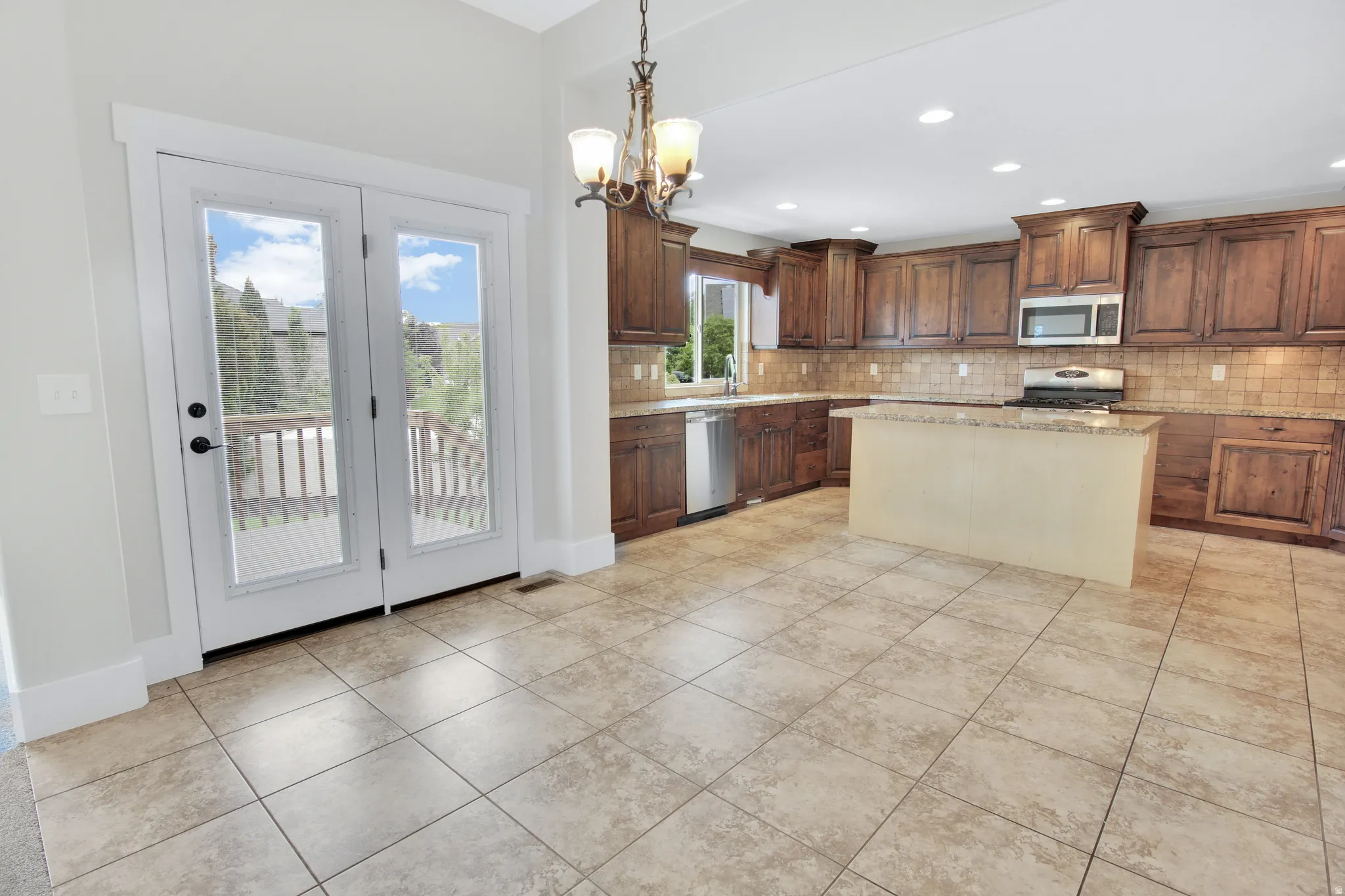 Spacious kitchen featuring warm wood cabinetry, stainless steel appliances, a central island with countertop, and tile flooring