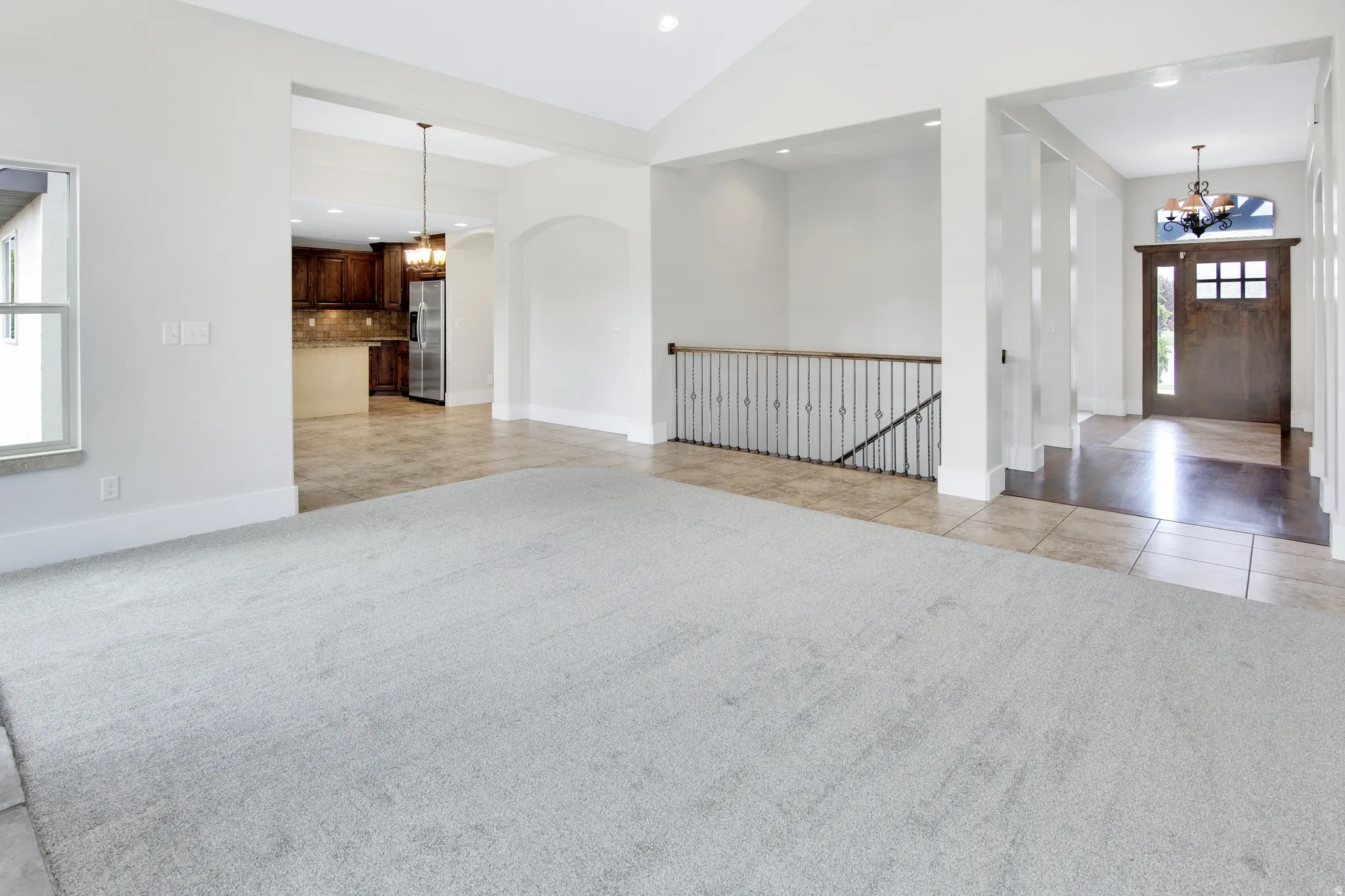 Vaulted ceiling with recessed lighting, light gray carpeting, tile flooring, dark wood entry door with glass panes, and iron baluster railing