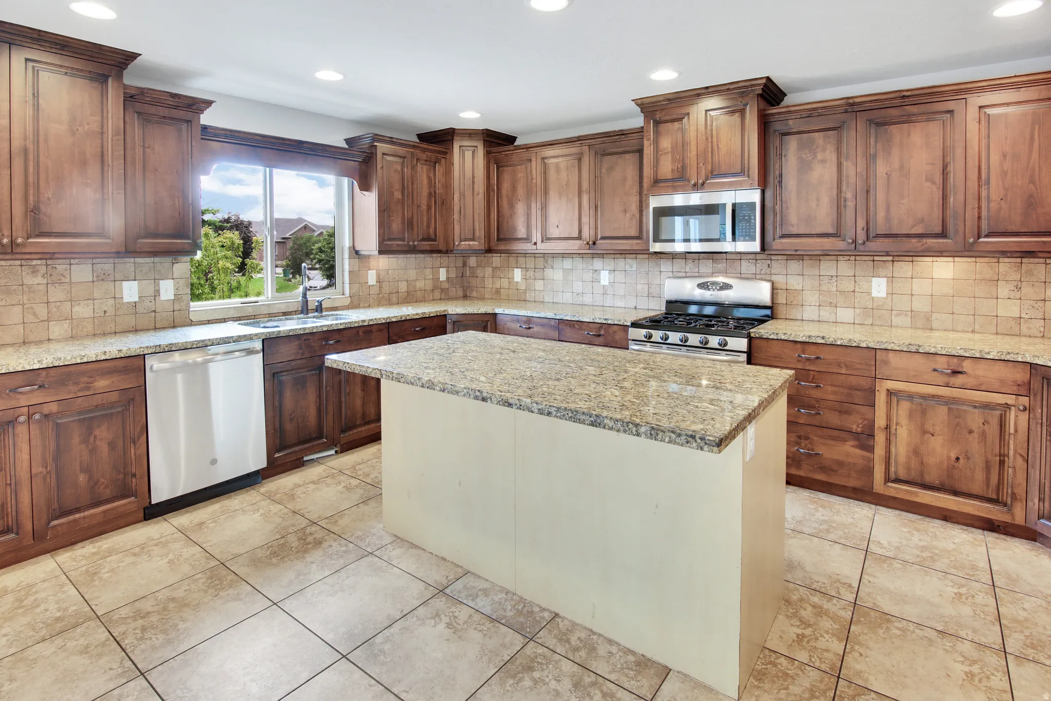 Kitchen featuring a granite island, wood-finish cabinetry, stainless steel appliances, tile backsplash, and recessed lighting