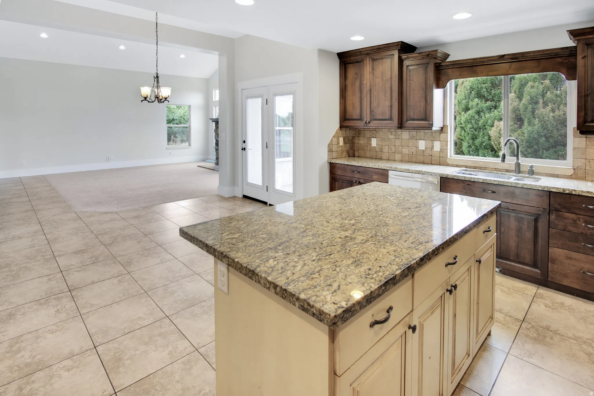 Kitchen island with a light granite countertop, tile flooring, rich wood-finish cabinetry, and a tile backsplash