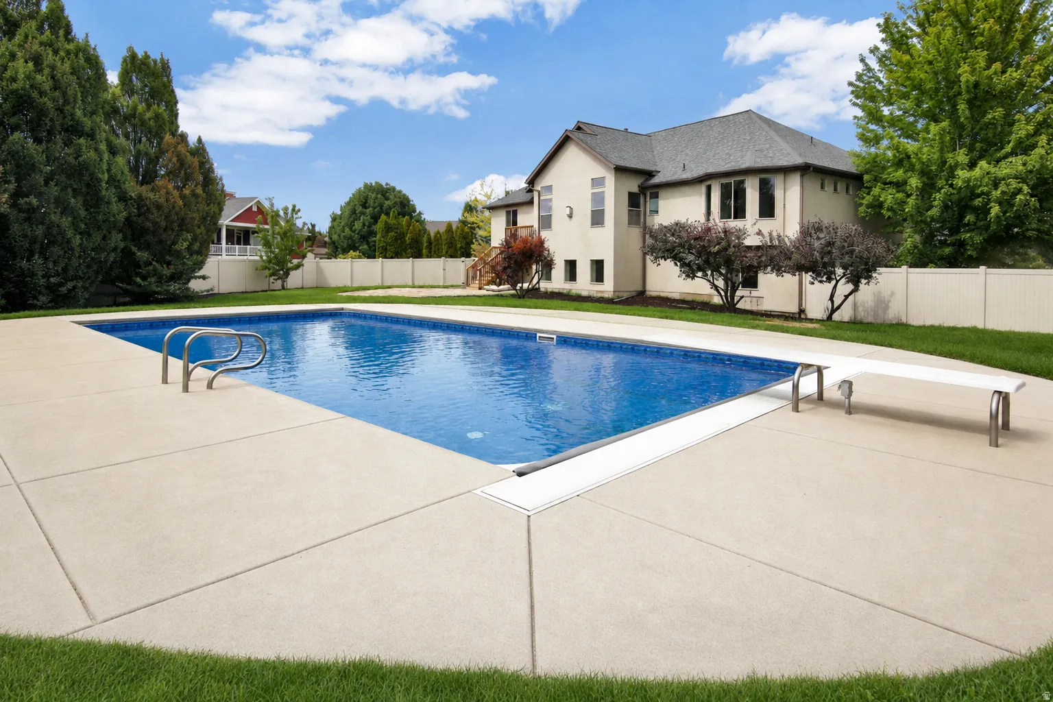 Expansive backyard featuring a large in-ground swimming pool with diving board, concrete surround, and privacy fencing