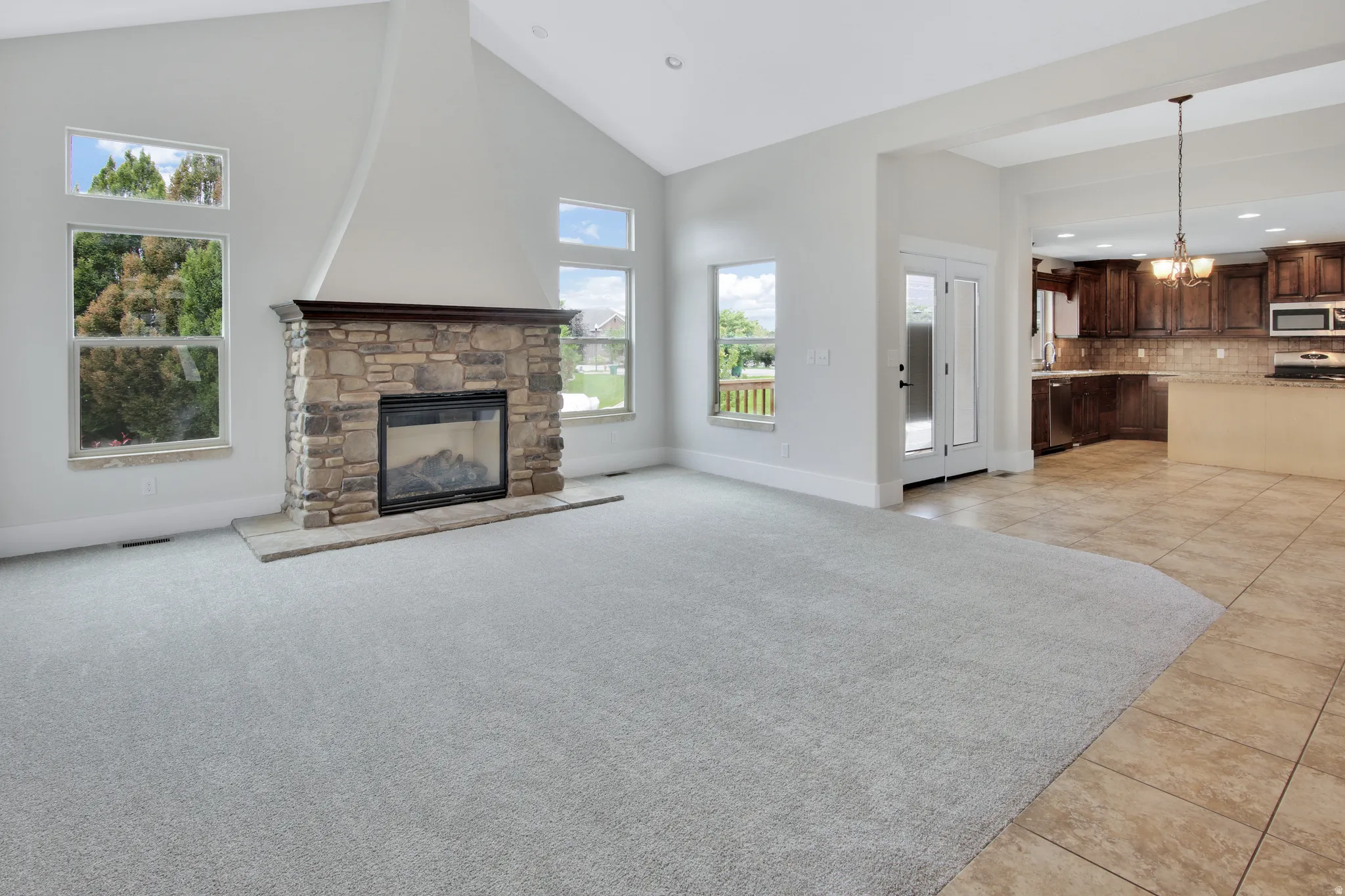 Vaulted ceiling, stone-clad fireplace, double French doors, wood-finish cabinetry, and tile flooring