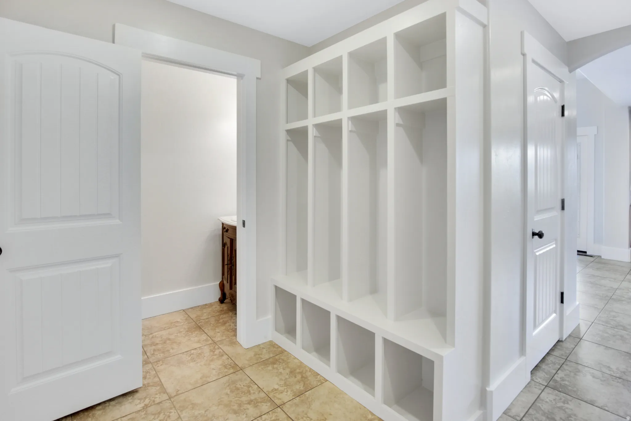 Built-in storage solutions with open cubbies and hooks, white paneled doors with black hardware, and tiled flooring