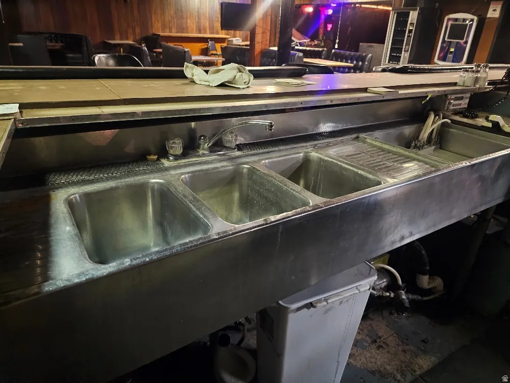 Stainless steel triple-compartment sink with integrated drainboard, chrome fixtures, and a bar counter