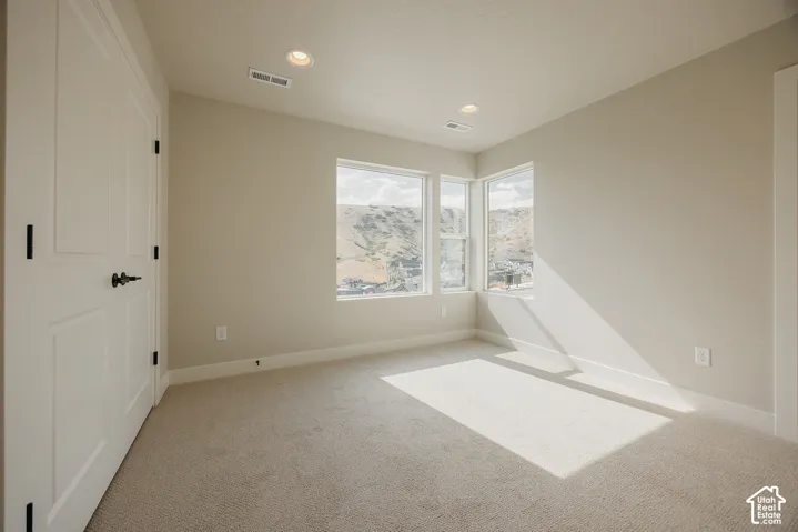 Recessed ceiling lighting, white two-panel doors with matte black hardware, corner window configuration, neutral carpeting, and painted walls