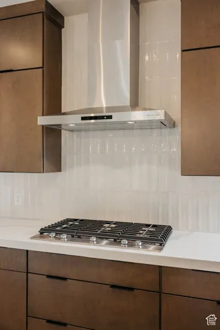 Stainless steel range hood, built-in gas cooktop, light-toned countertop, and dark wood-finish cabinetry with linear hardware