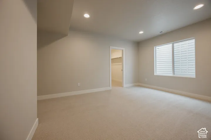 Recessed lighting, neutral wall paint, light-colored carpeting, window with privacy blinds, and an open doorway to a closet with shelving