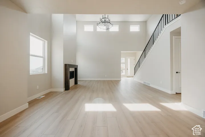 Two-story ceiling height, fireplace with a dark wood-finish surround, wood-finish flooring, staircase with black metal balusters, and a contemporary chandelier