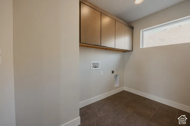 Laundry space featuring upper cabinetry, a mounted clothes rod, a rectangular window, and neutral-toned floor tiling