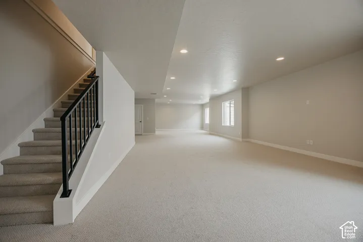Expansive carpeted area with recessed lighting, multiple windows, and a staircase featuring a black metal railing