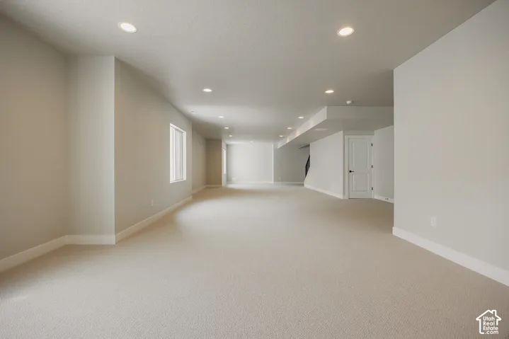 Expansive carpeted area featuring recessed lighting, multiple windows, and a panel door with a black handle