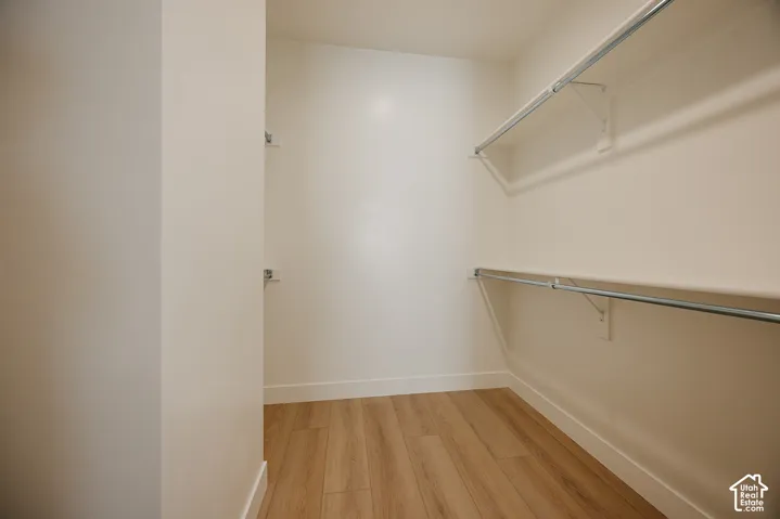 Walk-in closet with wood-finish flooring, white walls, and built-in shelving