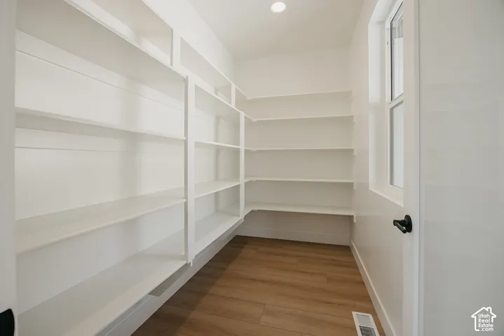 Expansive pantry featuring extensive built-in shelving, wood-finish flooring, recessed lighting, and a window