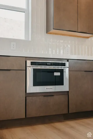 Built-in microwave, wood-finish cabinetry, light countertop, and a white subway tile backsplash