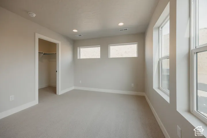 Soft gray carpet, recessed ceiling lighting, multiple windows, and an integrated closet with shelving