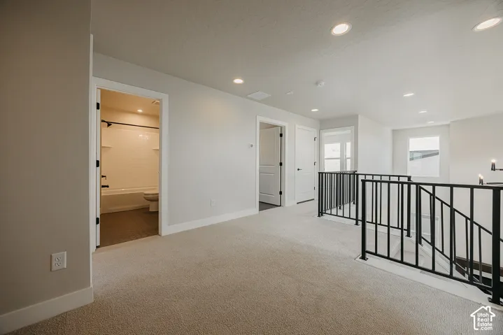 Carpeted open landing with black metal railing, recessed lighting, and white trim