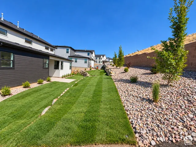 Expansive backyard featuring a manicured lawn, a concrete patio, and a rock-landscaped area with mature plantings