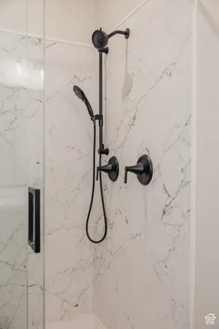 Shower enclosure featuring marble-patterned wall panels, a matte black dual-function shower system, and a glass shower door with a matte black handle