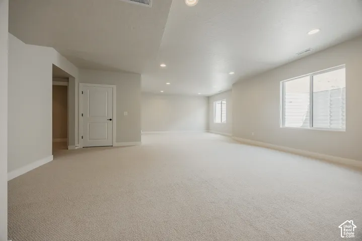 Expansive carpeted area with recessed lighting, two white-trimmed windows, and a panel door with dark hardware