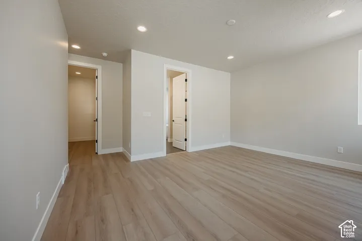 Recessed lighting, light-toned wood-finish flooring, white walls, white trim, and interior doors with dark hardware