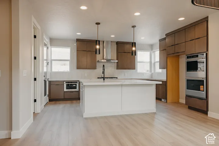 Gourmet kitchen with light wood-finish flooring, white countertops, built-in stainless steel appliances, and dark wood cabinetry