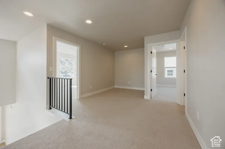 Carpeted landing area featuring recessed lighting, a black metal railing, and white trim