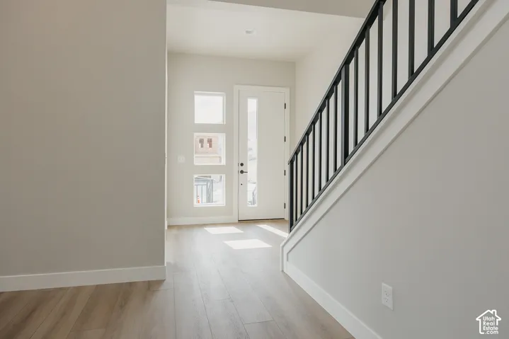 Entryway featuring wood-finish flooring, a white paneled entry door with sidelights, a contemporary black metal staircase railing, and light gray wall finishes