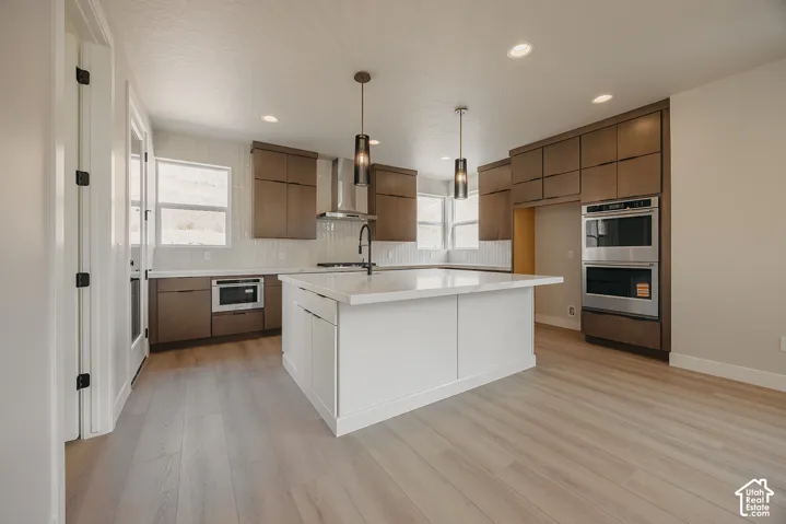 Kitchen featuring a white island with an integrated sink, wood-finish flooring, recessed lighting, and stainless steel appliances