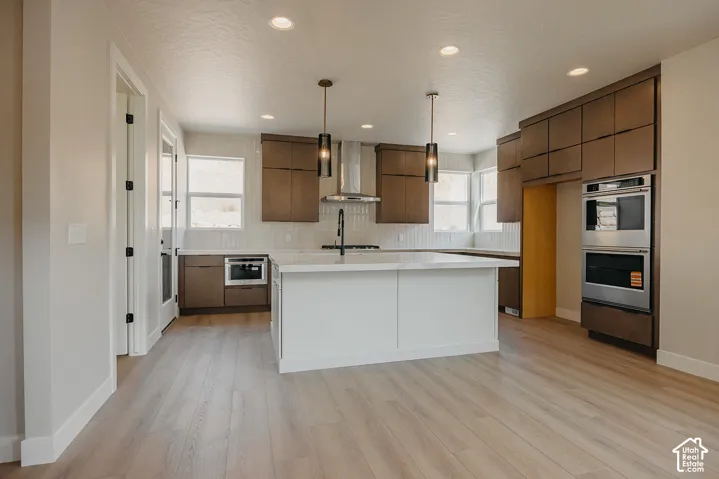 Modern kitchen featuring wood-finish flooring, a central island with a white countertop, two pendant lights, and built-in stainless steel appliances