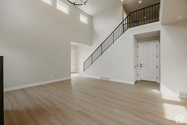 Soaring ceilings with transom windows, wood-finish flooring, a two-story staircase with black iron balusters, and a contemporary chandelier