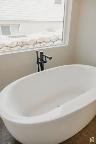 Freestanding soaking tub with matte black floor-mounted faucet, large window, and dark-toned floor tiling