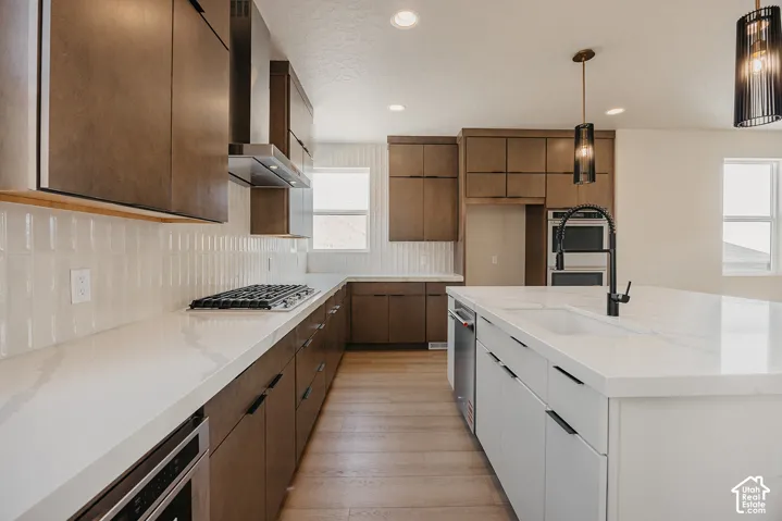 Modern kitchen featuring rich wood cabinetry, white quartz countertops, stainless steel appliances, white subway tile backsplash, and warm wood-finish flooring throughout the galley layout with pendant lighting and recessed ceiling fixtures
