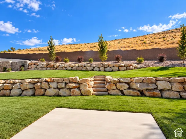 Tiered landscaping with natural stone retaining walls, concrete patio, and manicured lawns