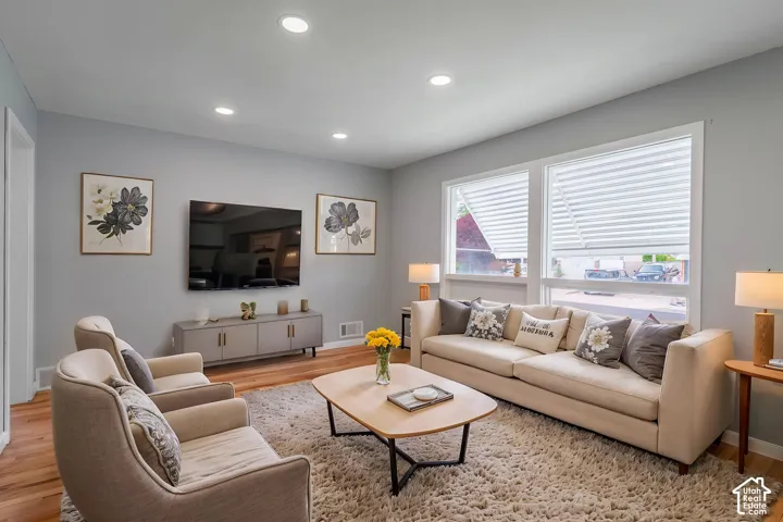 Living area featuring wood-finish flooring, recessed lighting, and large windows with integrated blinds