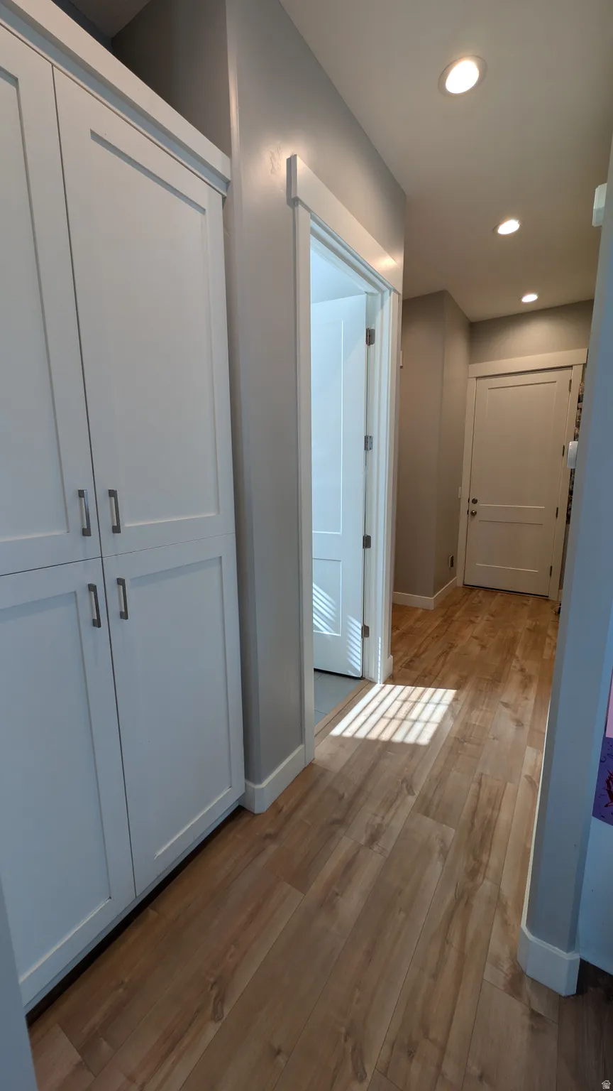Hallway featuring extensive built-in white panel cabinetry, wood-finish flooring, recessed lighting, and white baseboards