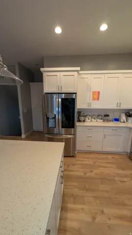 Contemporary kitchen featuring light wood-finish flooring, white shaker cabinetry with brushed nickel hardware, and speckled light-toned countertops