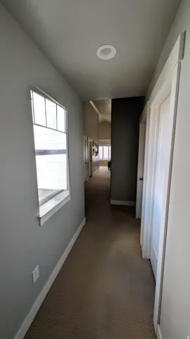 Carpeted hallway with a window, recessed lighting, and white trim
