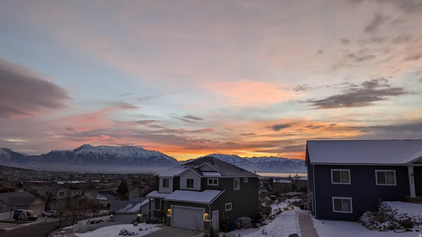 Panoramic mountainous scenery with a distant body of water, framed by a vibrant sunset sky