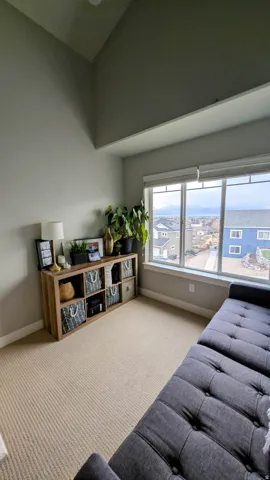 Vaulted ceiling room featuring large windows, beige carpeting, and a built-in wood-finish shelving unit