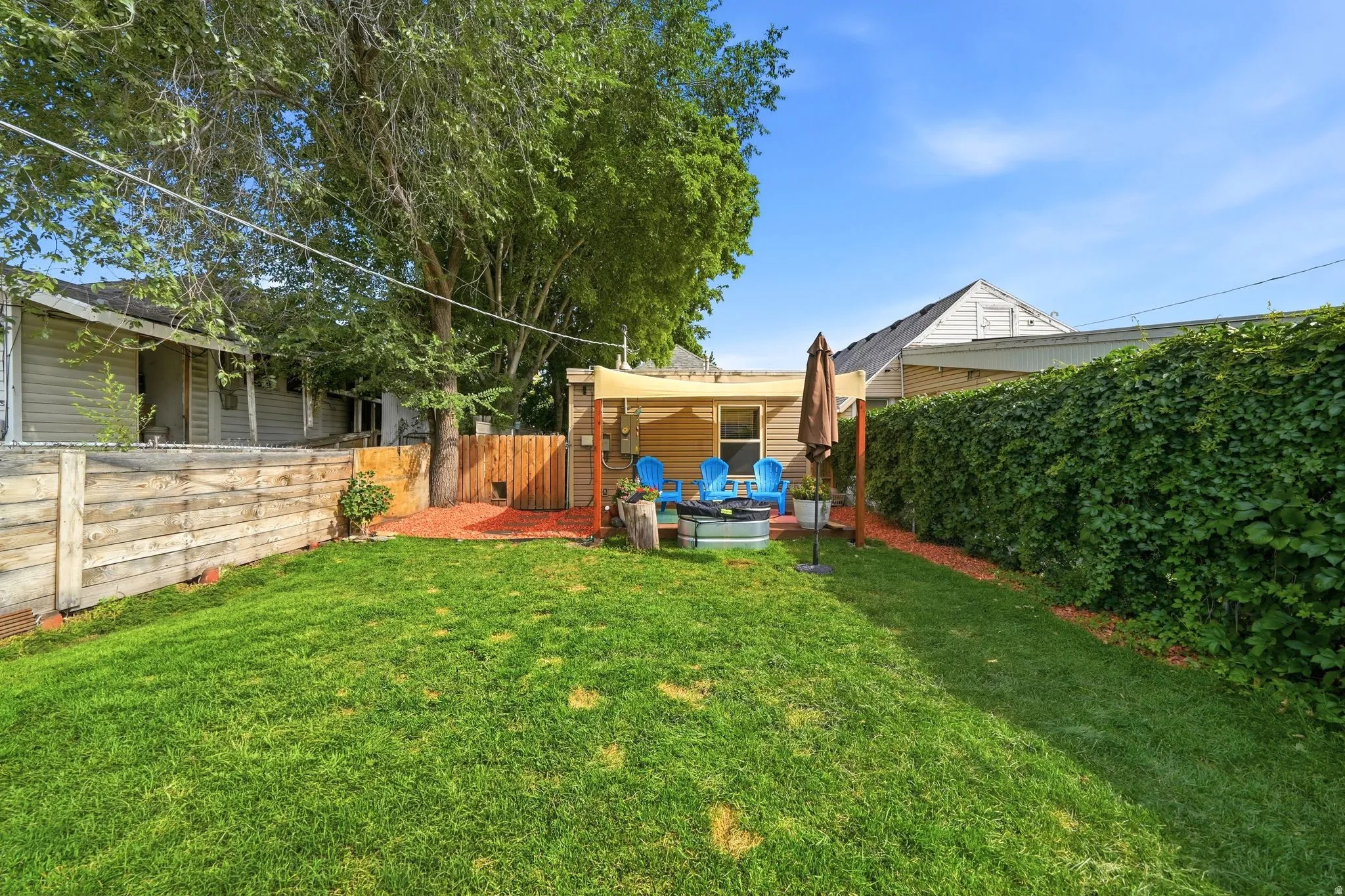 Expansive lawn with a wooden fence, mature tree, and a paved patio area