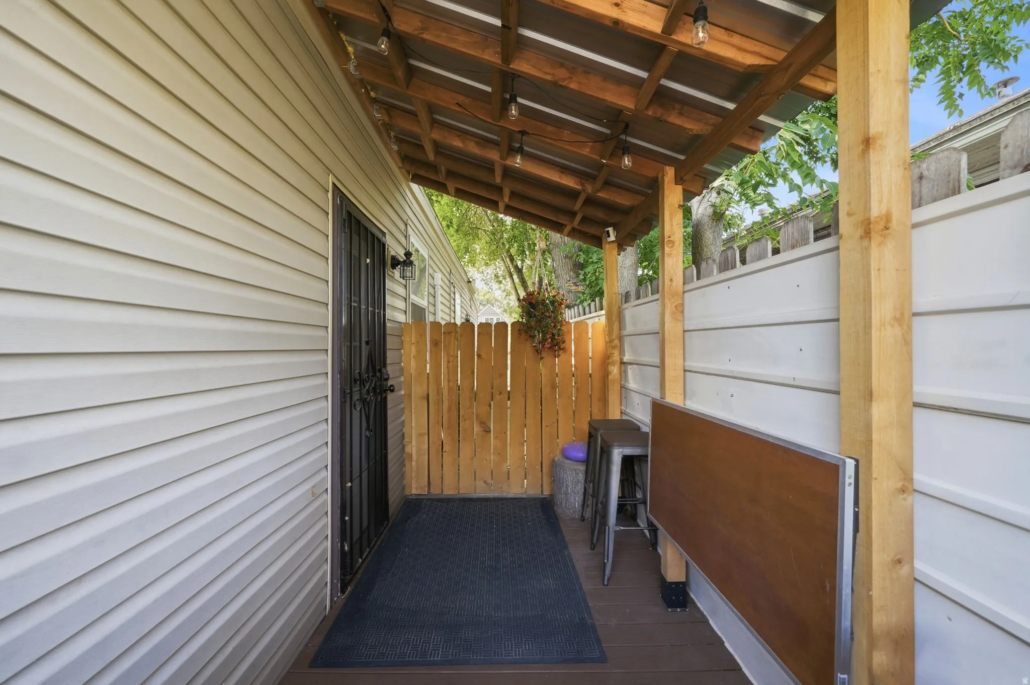 Covered porch area with wood-finish decking, light-colored siding, and a wooden privacy fence