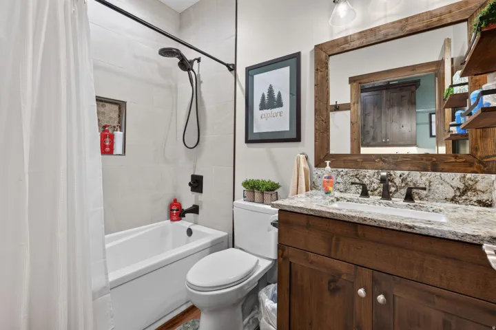 Tub and shower combination featuring black fixtures, a tiled shower surround, a built-in shower niche, and a vanity with a granite countertop and wood-finish cabinetry