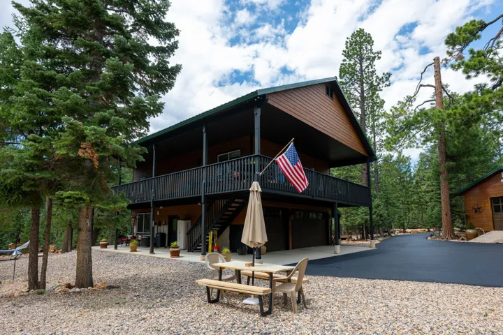 Two-story cabin-style residence featuring a wood-panel exterior, an expansive upper-level balcony with black railing, and a lower-level covered patio