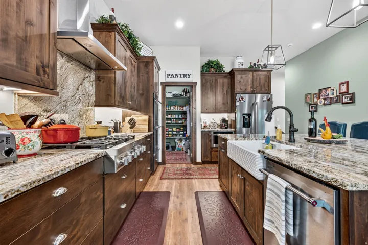 Kitchen featuring wood-finish cabinetry, stone slab countertops, stainless steel appliances, a farmhouse sink, and wood-finish flooring