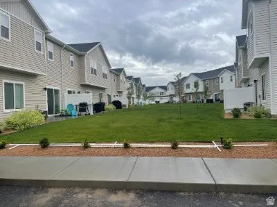 Neutral-toned siding, dark shingle roofing, sliding patio door, concrete patio, and a manicured lawn