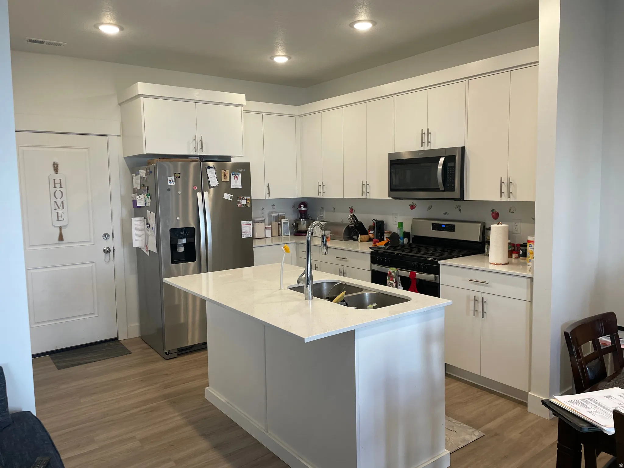 Kitchen featuring a center island with sink, stainless steel appliances, recessed lighting, white cabinetry, and wood-finish flooring