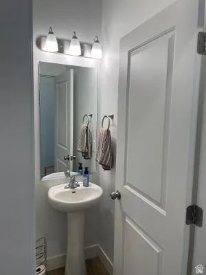 Pedestal sink with chrome faucet, wall-mounted mirror, and a three-light vanity fixture
