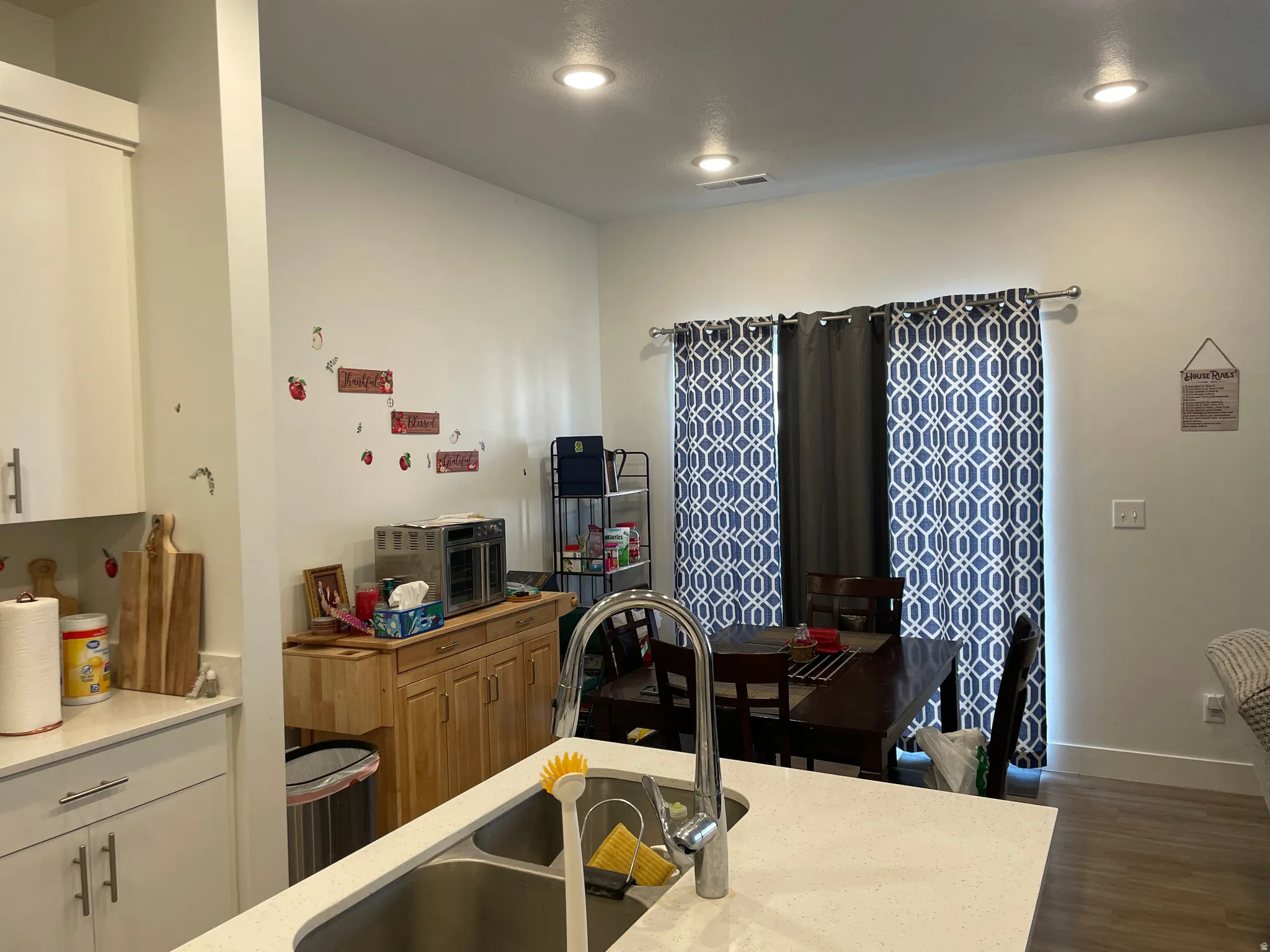 Open-concept kitchen and living area featuring white cabinetry, quartz countertop, stainless steel faucet, recessed lighting, and wood-finish flooring throughout