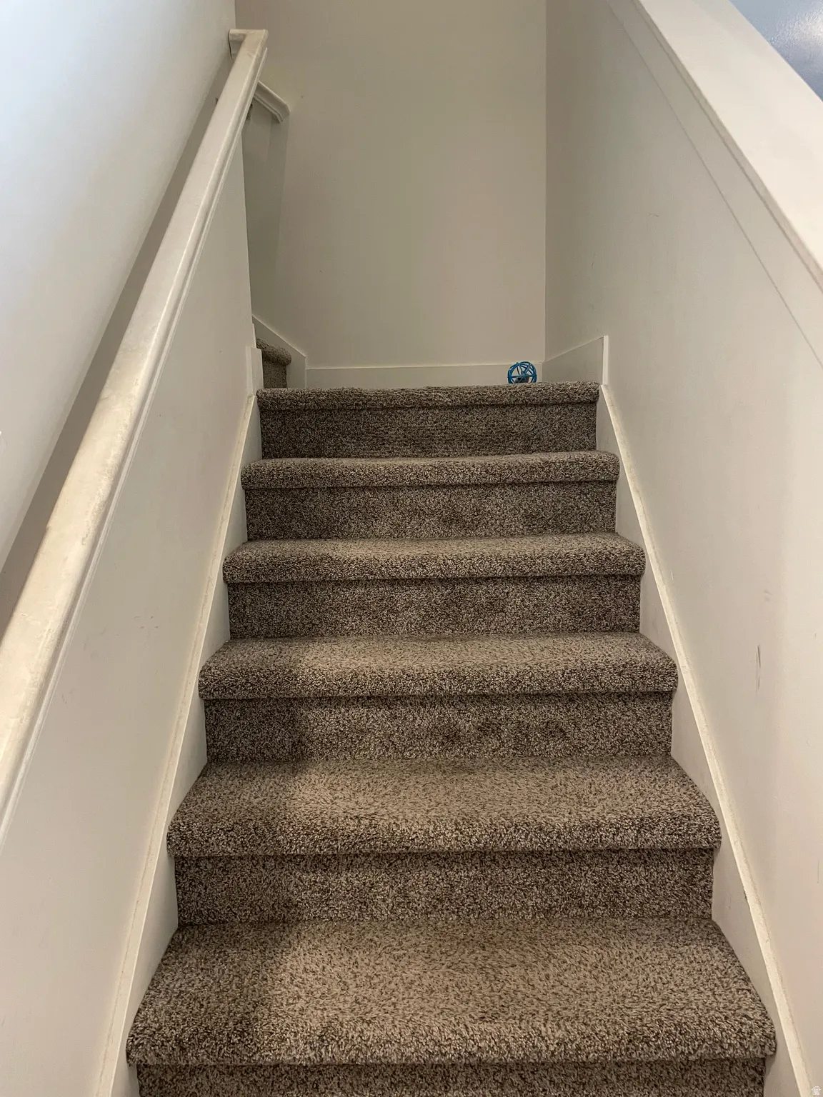 Carpeted staircase featuring neutral toned treads and a clean white painted wall with coordinating handrail for secure passage between levels
